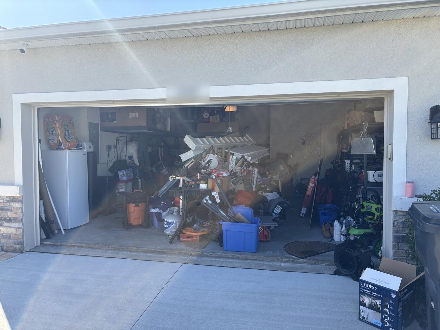 Two-car garage packed wall to wall with boxes, tools, a propane tank, and bins before the cleanout