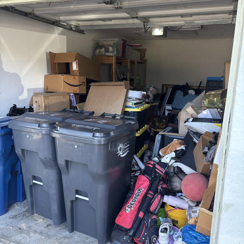 One-car garage before, with boxes, bags, and sports gear piled to the door