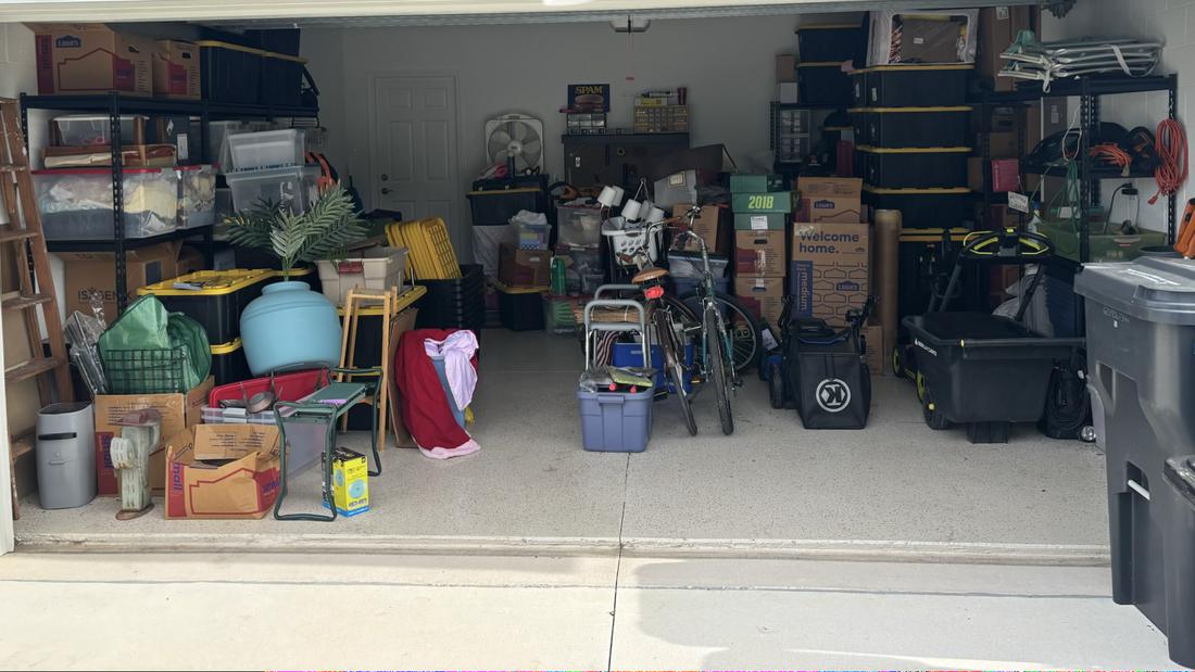 Two-car garage before, packed with boxes, bins, bikes, and lawn equipment